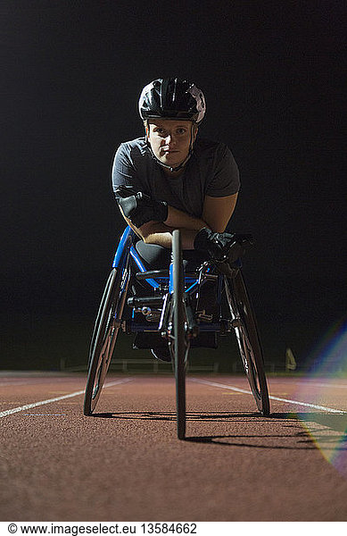 Portrait determined  tough young female paraplegic athlete training for wheelchair race on sports track at night