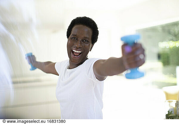 Portrait energetic mature woman exercising with dumbbells at home