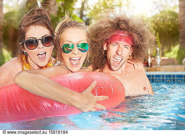 Portrait exuberant  playful young friends with inflatable raft in summer swimming pool