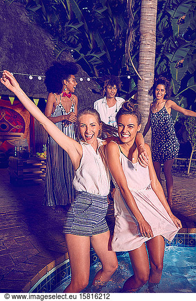 Portrait exuberant young women friends partying  dancing and wading at pool party