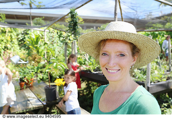 Portrait f smiling woman wearing sunhat in greenhouse  children in background