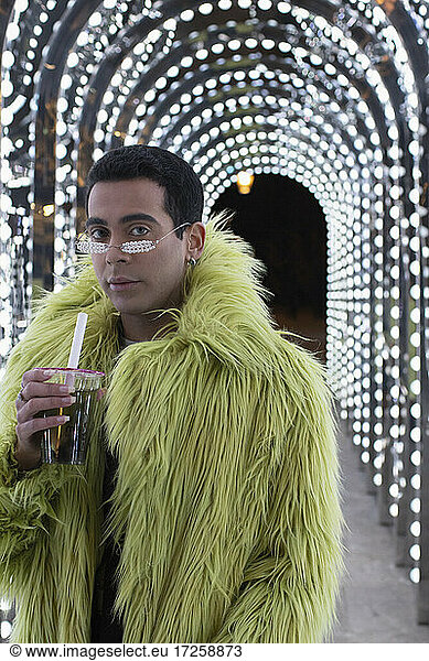 Portrait fashionable young man in green fur coat under arch lights