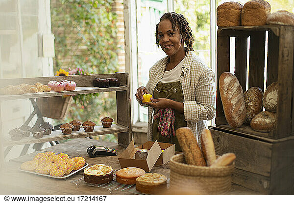 Portrait female baker arranging display in shop