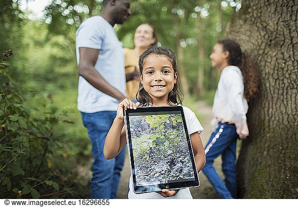 Portrait girl holding digital tablet with photograph of plant in woods