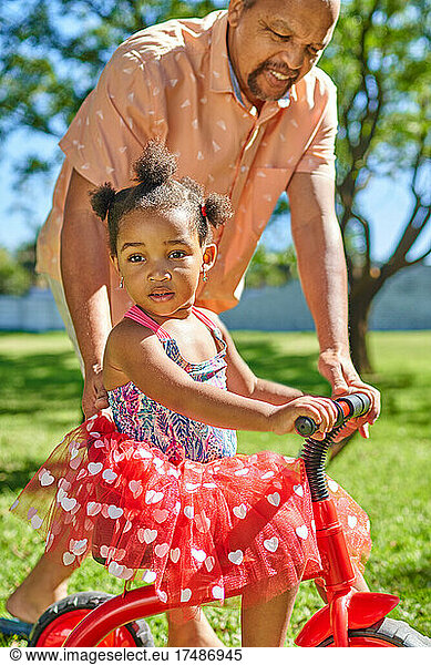 Portrait grandfather pushing cute granddaughter on tricycle in park