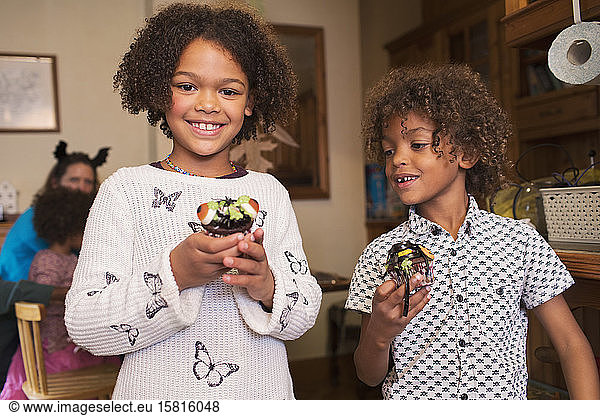 Portrait happy brother and sister with decorated Halloween cupcakes