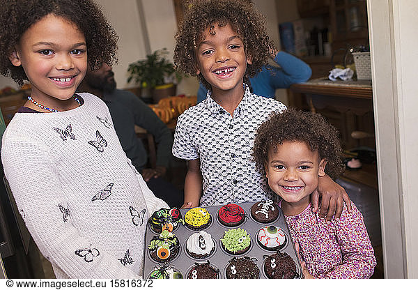 Portrait happy brother and sisters with decorated Halloween cupcakes