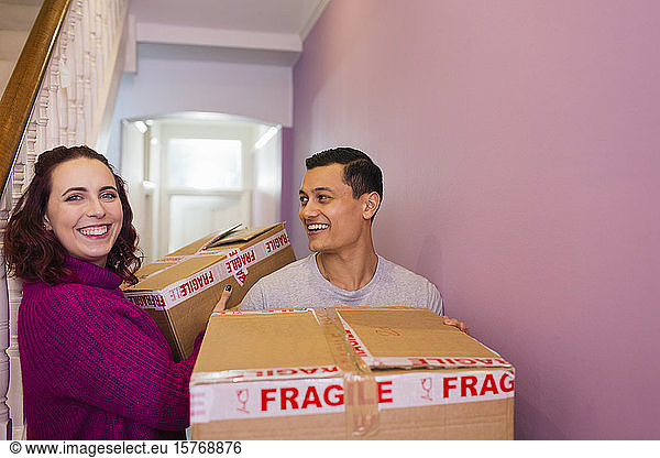 Portrait happy couple moving house  carrying cardboard boxes in corridor