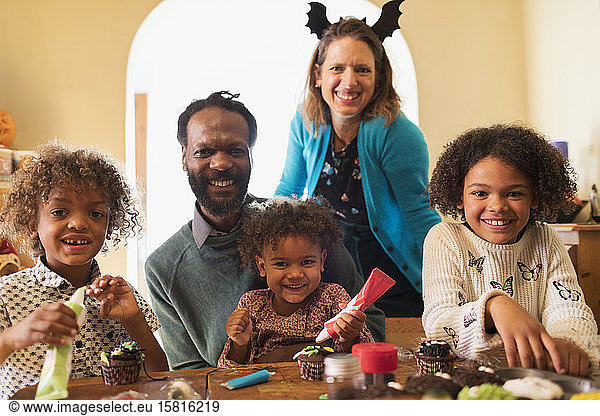Portrait happy family decorating Halloween cupcakes at table