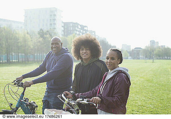 Portrait happy family with bicycles in sunny urban park grass