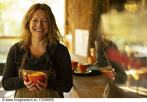 Portrait happy female coffee shop owner with cappuccino