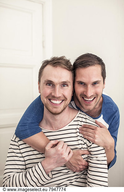 Portrait happy gay man embracing partner from behind at home