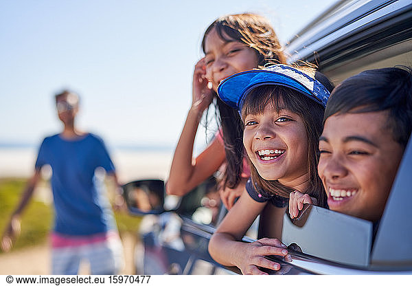 Portrait happy kids leaning out sunny car window