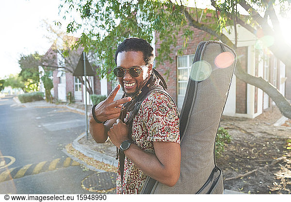 Portrait happy male musician with guitar case gesturing peace sign