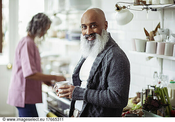 Portrait happy mature man with beard drinking coffee in kitchen