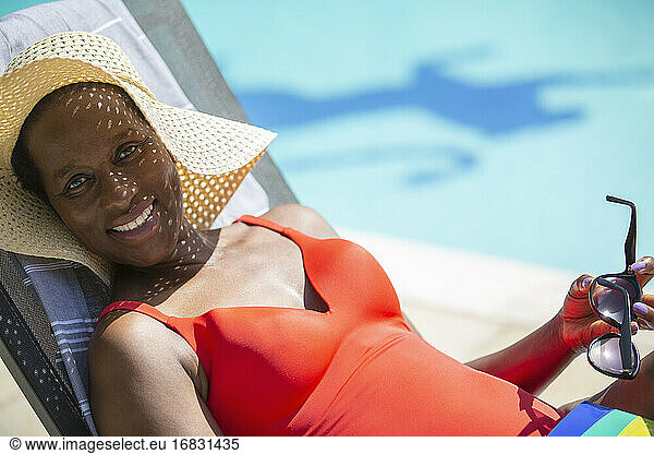 Portrait happy mature woman in sun hat sunbathing at sunny poolside
