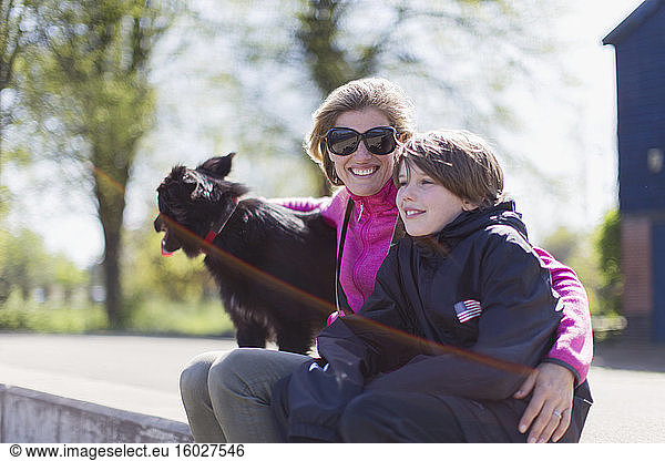 Portrait happy mother and son with dog on sunny ledge