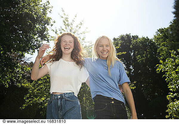 Portrait happy preteen girl friends below sunny summer trees