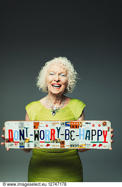 Portrait happy senior woman holding Dont Worry Be Happy license plates