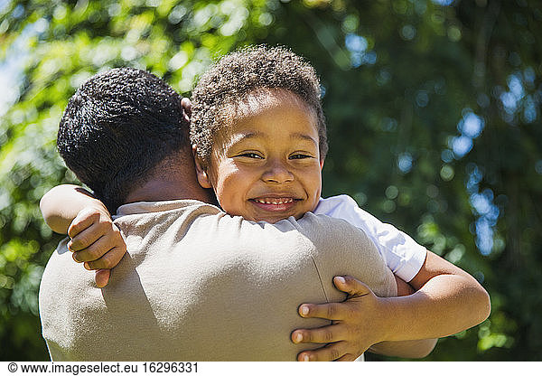 Portrait happy son hugging father in sunshine