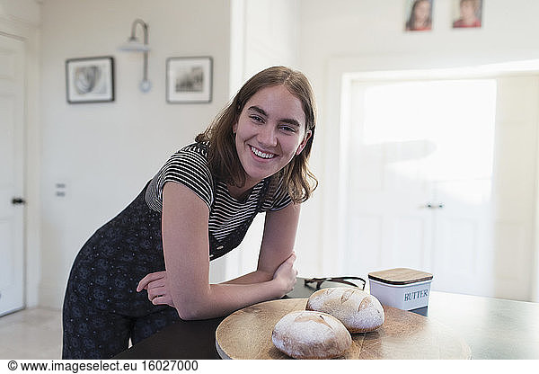 Portrait happy teenage girl with homemade baked bread in kitchen