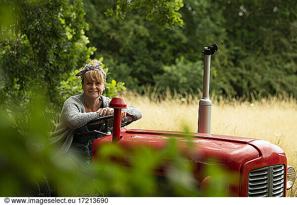 Portrait happy woman driving tractor in orchard