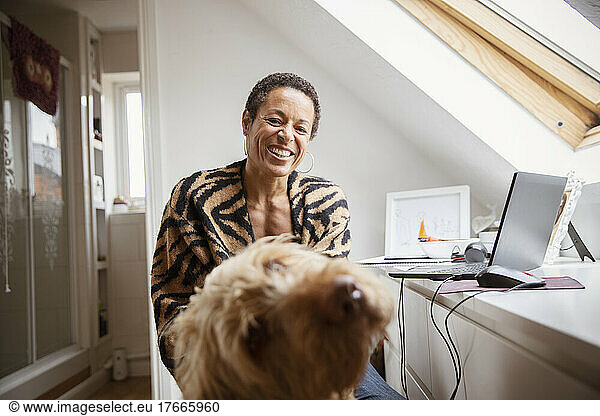 Portrait happy woman with dog at desk in home office