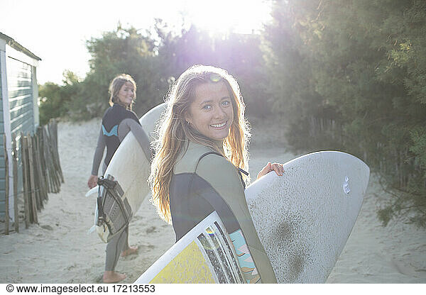 Portrait happy young female surfer with surfboard on sunny beach path