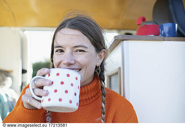 Portrait happy young woman drinking tea in camper van