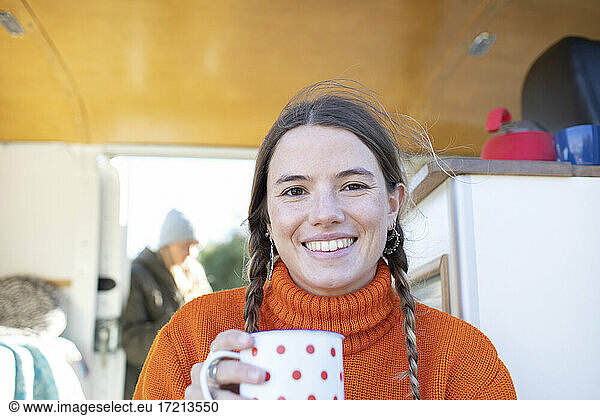 Portrait happy young woman drinking tea in camper van doorway