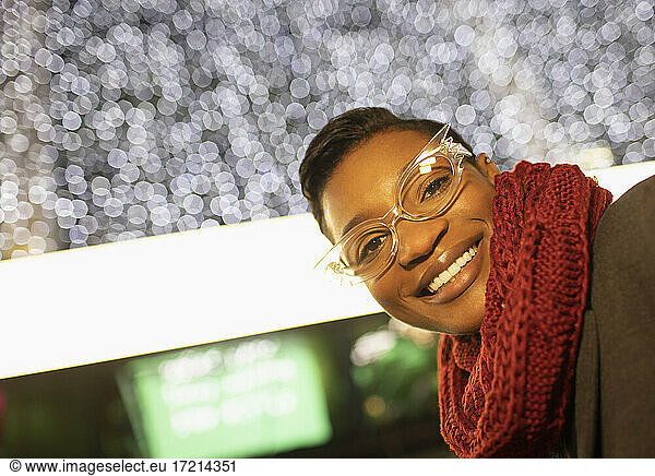 Portrait happy young woman in funky eyeglasses and scarf below lights