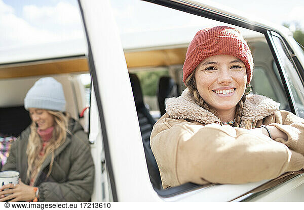 Portrait happy young woman on road trip at van window