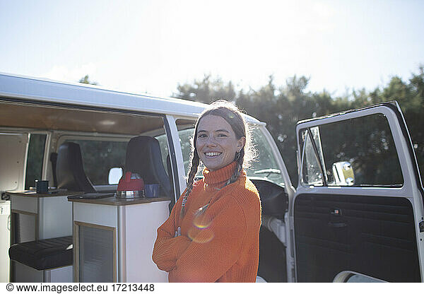 Portrait happy young woman outside sunny camper van