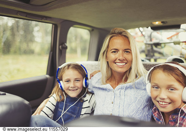 Portrait lächelnde Mutter und Töchter mit Kopfhörer auf dem Rücksitz des Autos