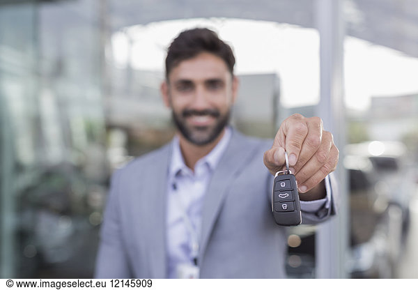 Portrait lächelnder  selbstbewusster Autoverkäufer mit neuen Autoschlüsseln