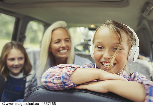 Portrait lächelndes Mädchen mit Kopfhörer auf dem Rücksitz des Autos