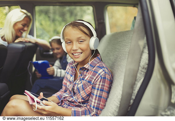 Portrait lächelndes Mädchen mit Kopfhörer mit digitalem Tablett auf dem Rücksitz des Autos