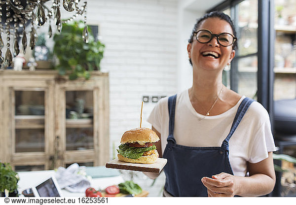 Portrait laughing woman holding cheeseburger on cutting board