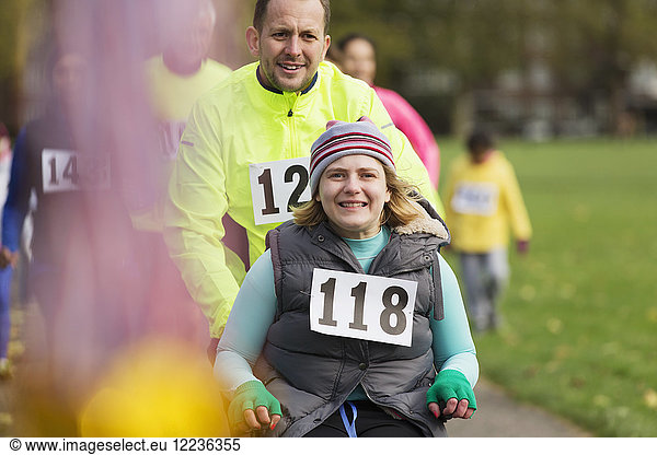 Portrait man pushing smiling woman in wheelchair at charity race in park