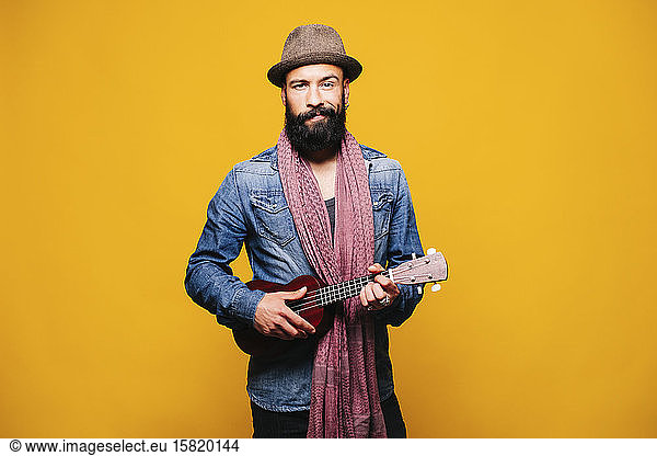 Portrait of a bearded young man in studio holding ukulele