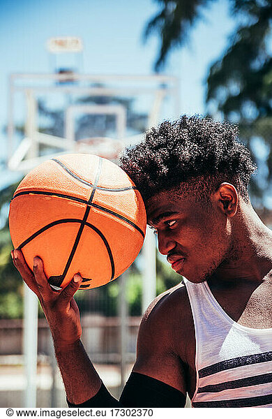 Portrait of a black African-American boy holding a basketball in his forehead on an urban basketball court.