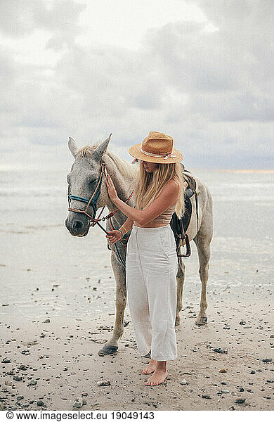 portrait of a blond girl posing at the beach with a withe horse