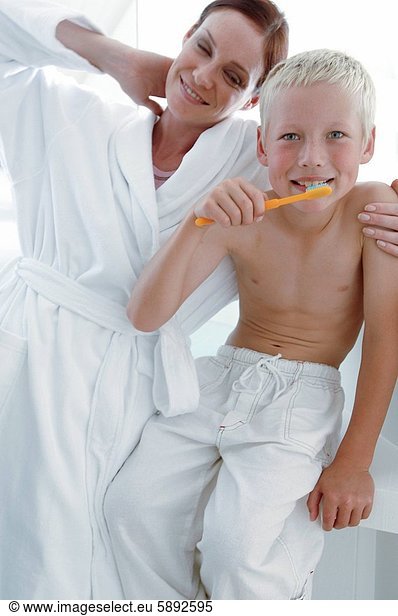 Portrait of a boy brushing teeth with his mother standing beside him