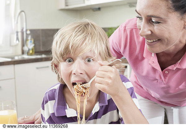 Portrait of a boy eating spaghetti with his mother