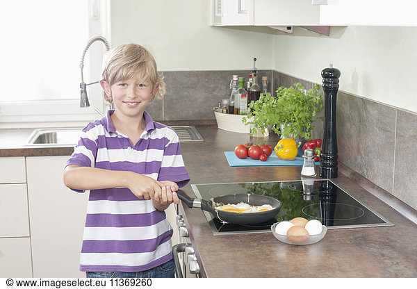 Portrait of a boy preparing fried eggs in kitchen