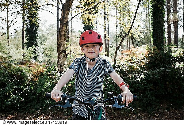 portrait of a boy smiling sat on his bike in the forest