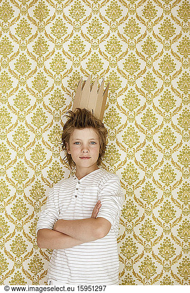 Portrait of a boy standing at a wall wearing cardboard crown