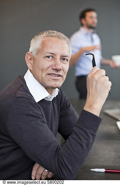 Portrait of a businessman holding glasses with colleague in background