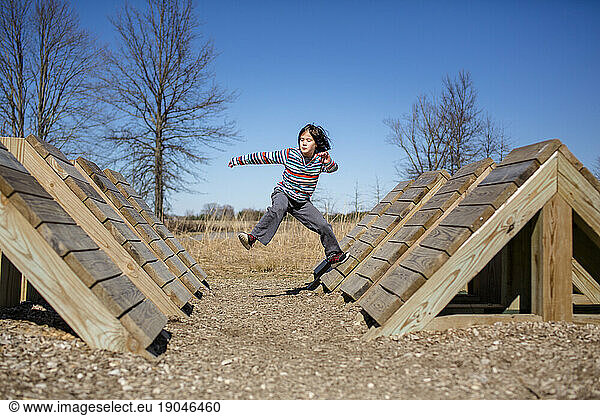 Portrait of a child mid-leap jumping across an obstacle course in park