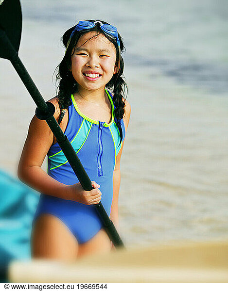 Portrait of a Chinese-American girl with a kayak on a sandy beach.